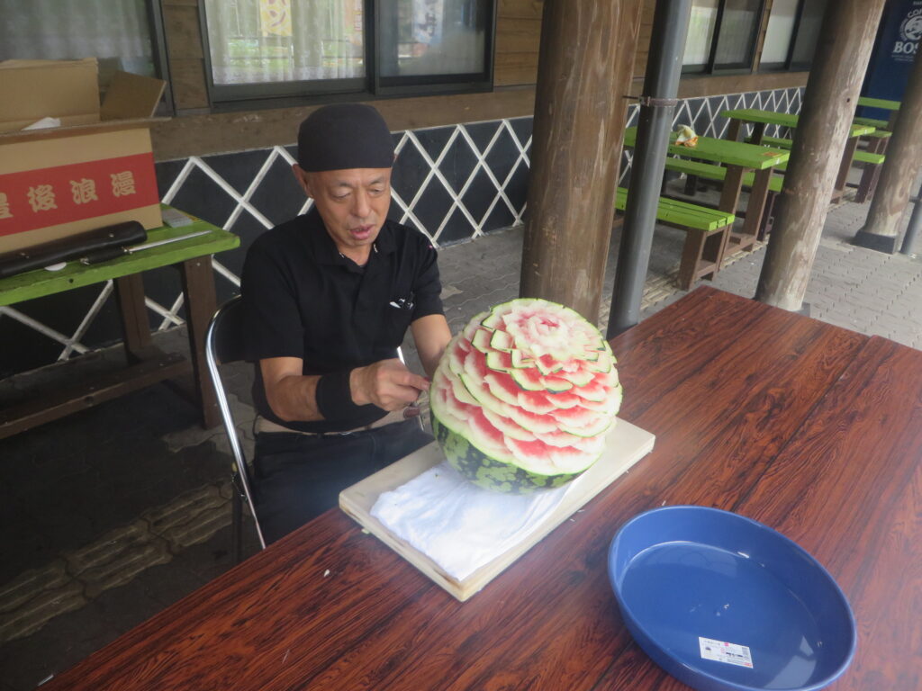 当駅の「北川はゆまレストラン」清水料理長によるスイカ彫刻開始から２時間経過。花の全体像がみえてきました。